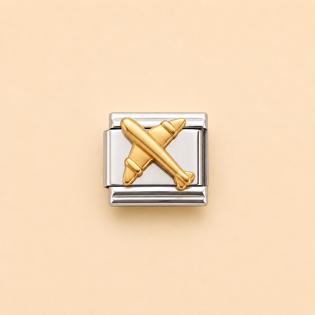 A two-tone Italian charm link featuring a polished gold airplane motif set against a silver-toned rectangular background, centered on a solid pale peach-beige backdrop.