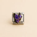A silver-toned rectangular charm link featuring a purple and black butterfly with gold outlines, set against a solid beige background.