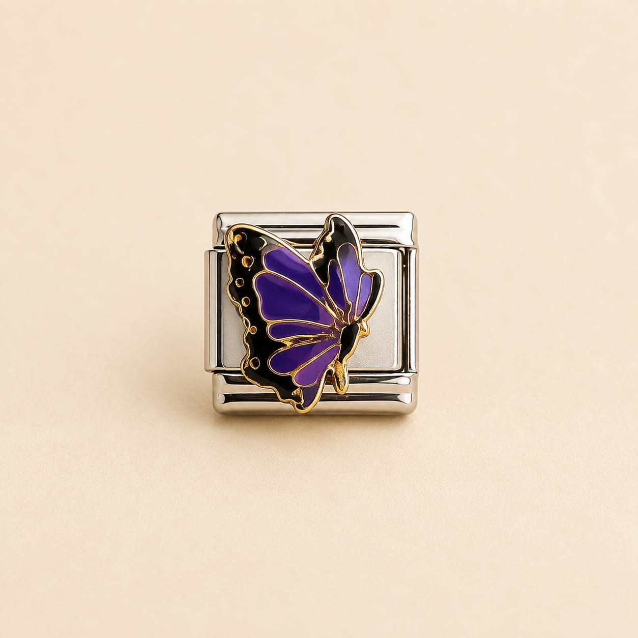 A silver-toned rectangular charm link featuring a purple and black butterfly with gold outlines, set against a solid beige background.