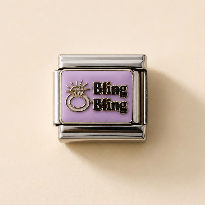 A rectangular charm link with a lavender purple face, featuring a gold-tone ring icon and the text 'Bling Bling' in black with a gold outline, set in polished silver-tone metal on a light beige background.