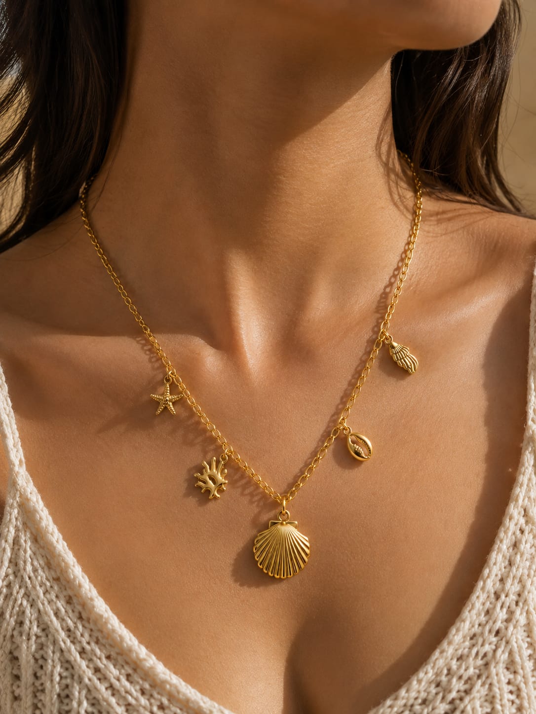 A gold necklace with seashell and starfish charms worn by a model in warm sunlight.