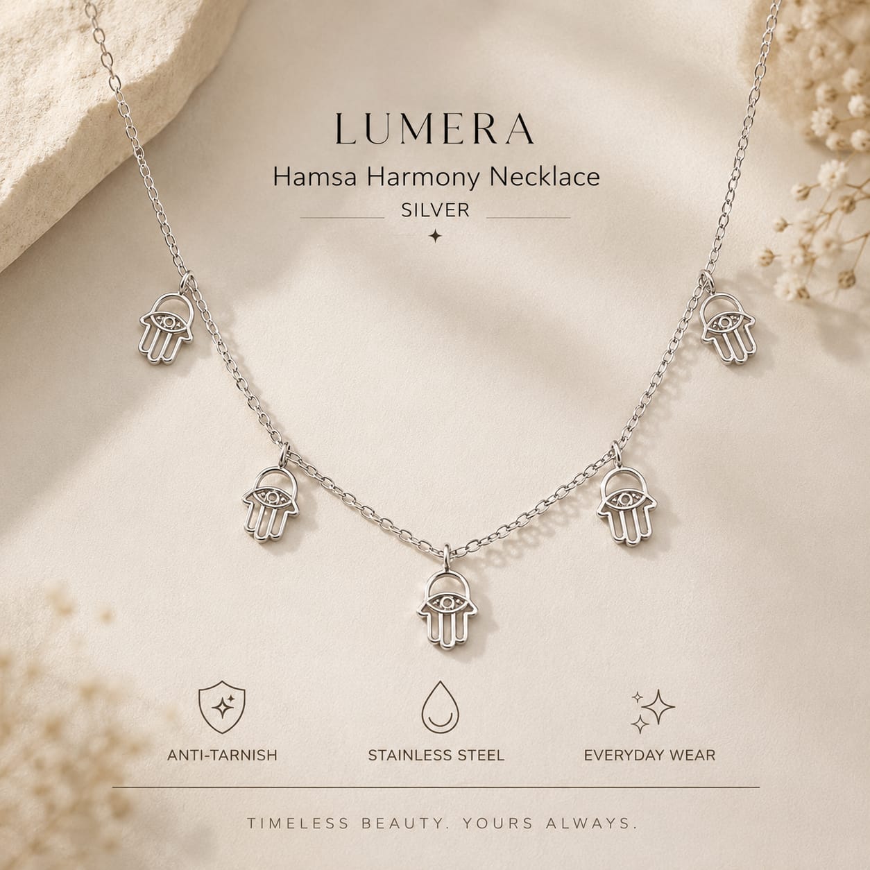 Silver Hamsa Harmony necklace with five hanging Hamsa charms, displayed on a soft beige background with decorative dried flowers and text reading 'LUMERA Hamsa Harmony Necklace SILVER'.