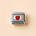 A rectangular silver-tone charm link featuring a light blue enamel background with a red heart and white angel wings, centered on a warm beige background.