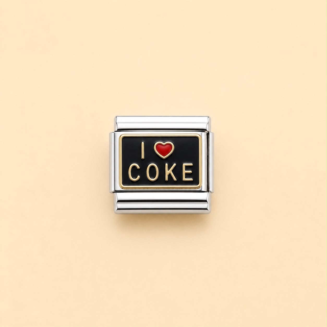 A rectangular silver-toned charm link with a black face, featuring the text 'I' and 'COKE' in gold-tone lettering and a small red heart symbol in the center, shown on a solid pale peach background.