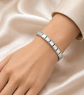 A close-up of a person's wrist wearing a polished silver Italian link bracelet, set against a soft beige satin fabric background.