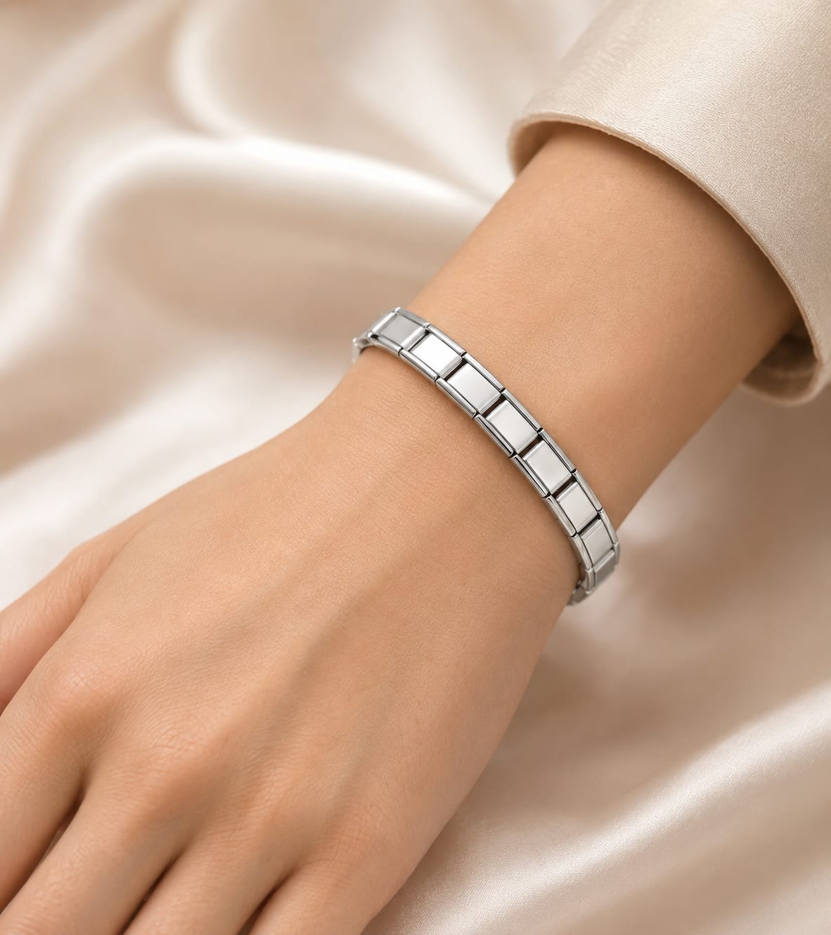 A close-up of a person's wrist wearing a polished silver Italian link bracelet, set against a soft beige satin fabric background.