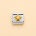 A silver-toned rectangular charm link featuring a textured gold star in the center, displayed on a solid pale peach background.