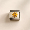 A square Italian charm link with a polished silver-tone metal frame and a central gold-tone ship's wheel emblem, displayed on a textured cream background.