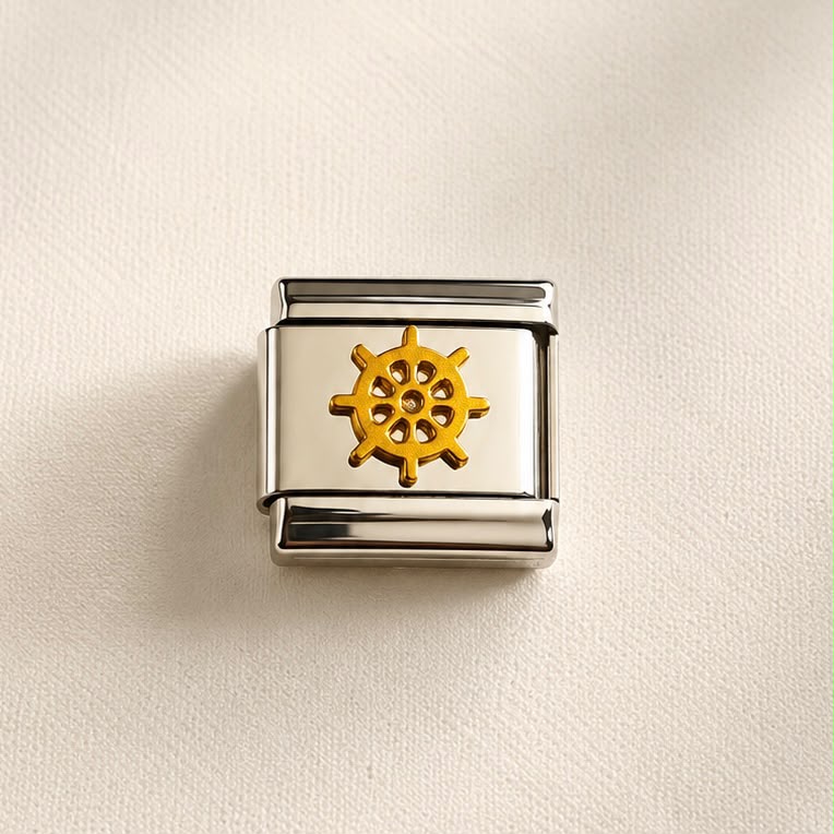 A square Italian charm link with a polished silver-tone metal frame and a central gold-tone ship's wheel emblem, displayed on a textured cream background.