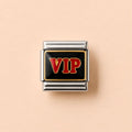 A square charm link featuring a black enamel center with the letters 'VIP' in red and gold, surrounded by a polished silver-tone metal border, set against a solid pale peach background.