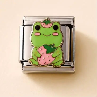A silver-toned Italian charm link featuring a cute green cartoon frog holding a pink strawberry, set against a solid light beige background.