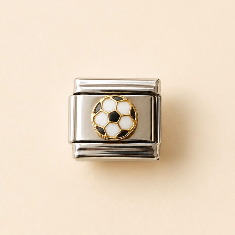 A square silver-toned metal charm link featuring a soccer ball motif in the center with white and black pentagons outlined in gold, set against a solid pale peach background.